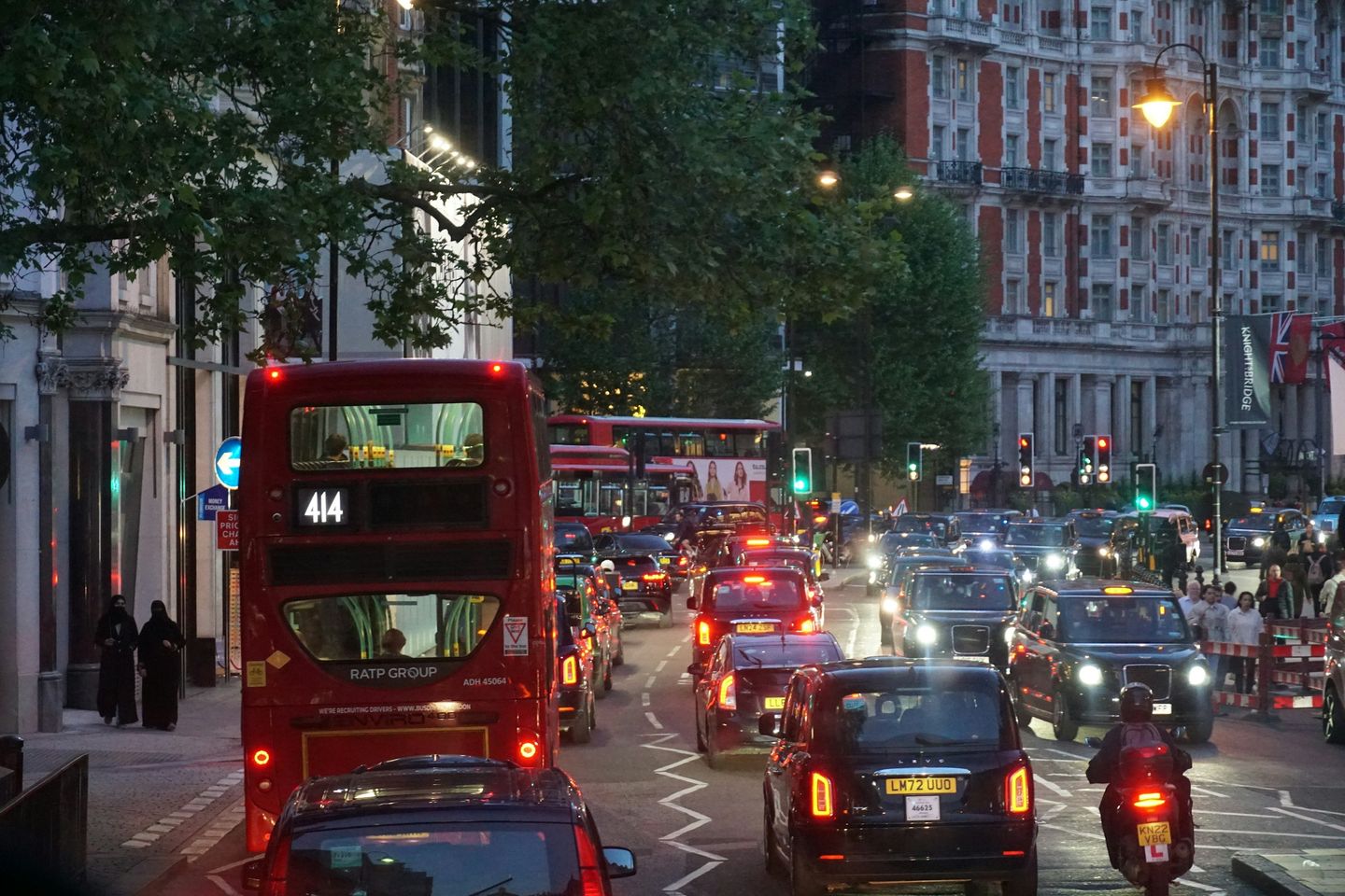 Evening traffic and red double-decker buses on a London street lined with tall Victorian buildings
