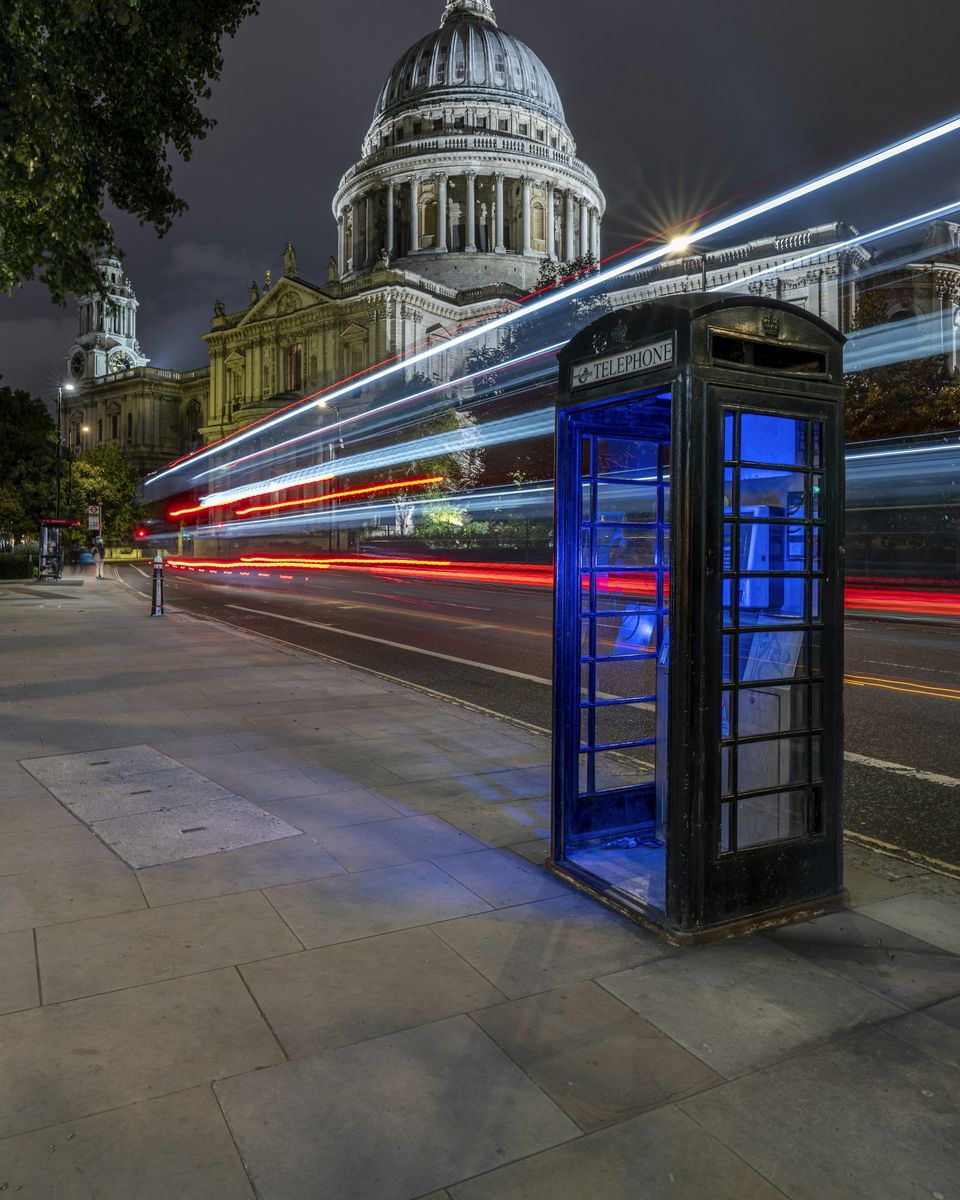 St Paul’s Cathedral at night with traffic light trails passing a red telephone box