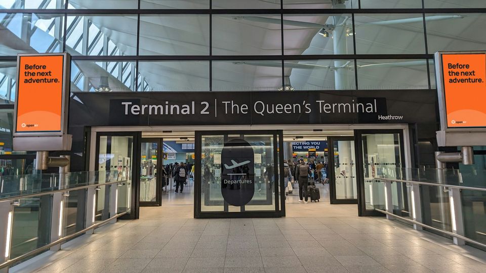The entrance to Heathrow Terminal 2 with two portrait screens showing an orange concept advert