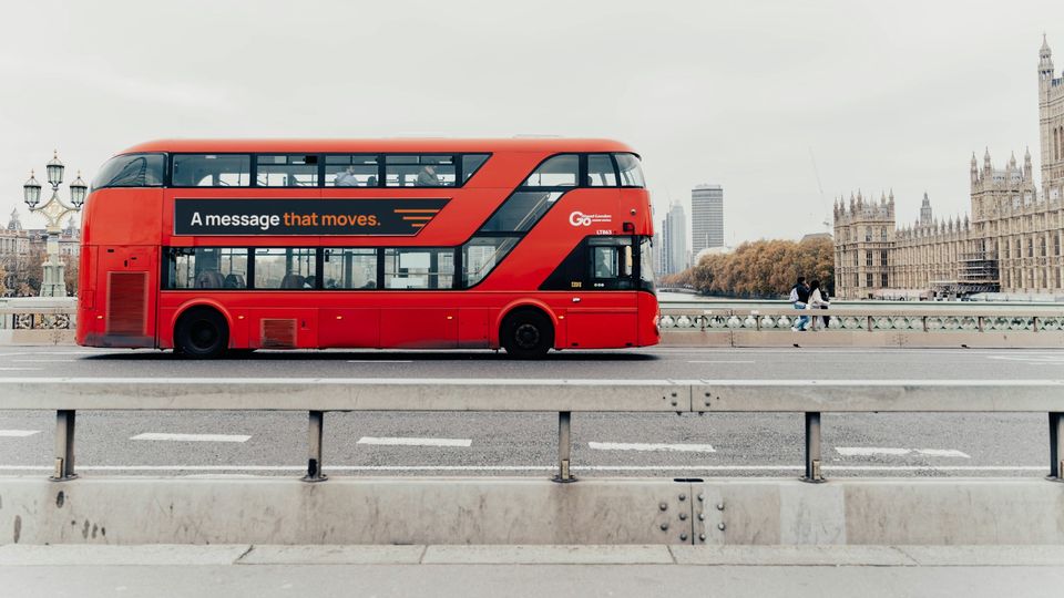 A red London double-decker on Westminster Bridge with an Open Air Media House concept on its side panel